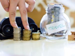 Travel budget - vacation money savings in a glass jar on world map. Collecting money for travel. Fingers stepping on the money.